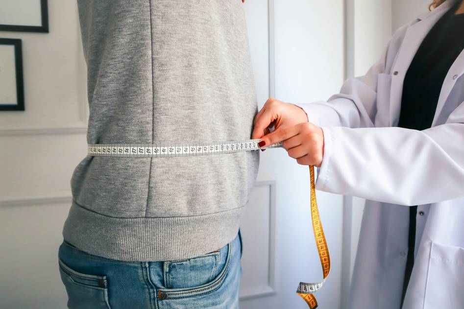 Woman measuring waist with tape in bright kitchen setting